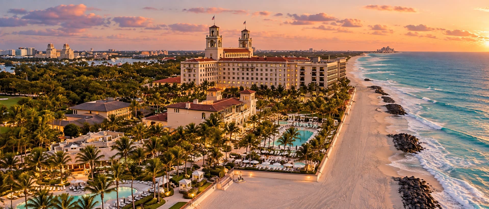 An oceanfront Palm Beach resort with twin bell towers at sunset, above palm gardens, pools and the beach