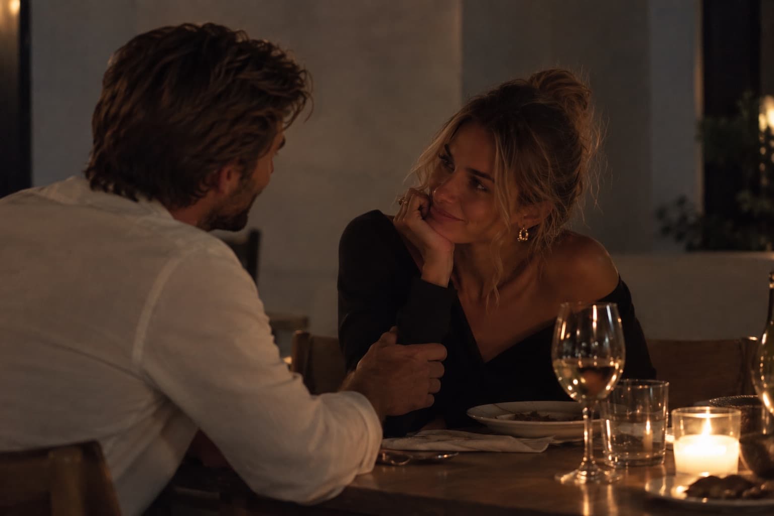 A woman resting her chin on her hand, smiling at the man across a dim candlelit table