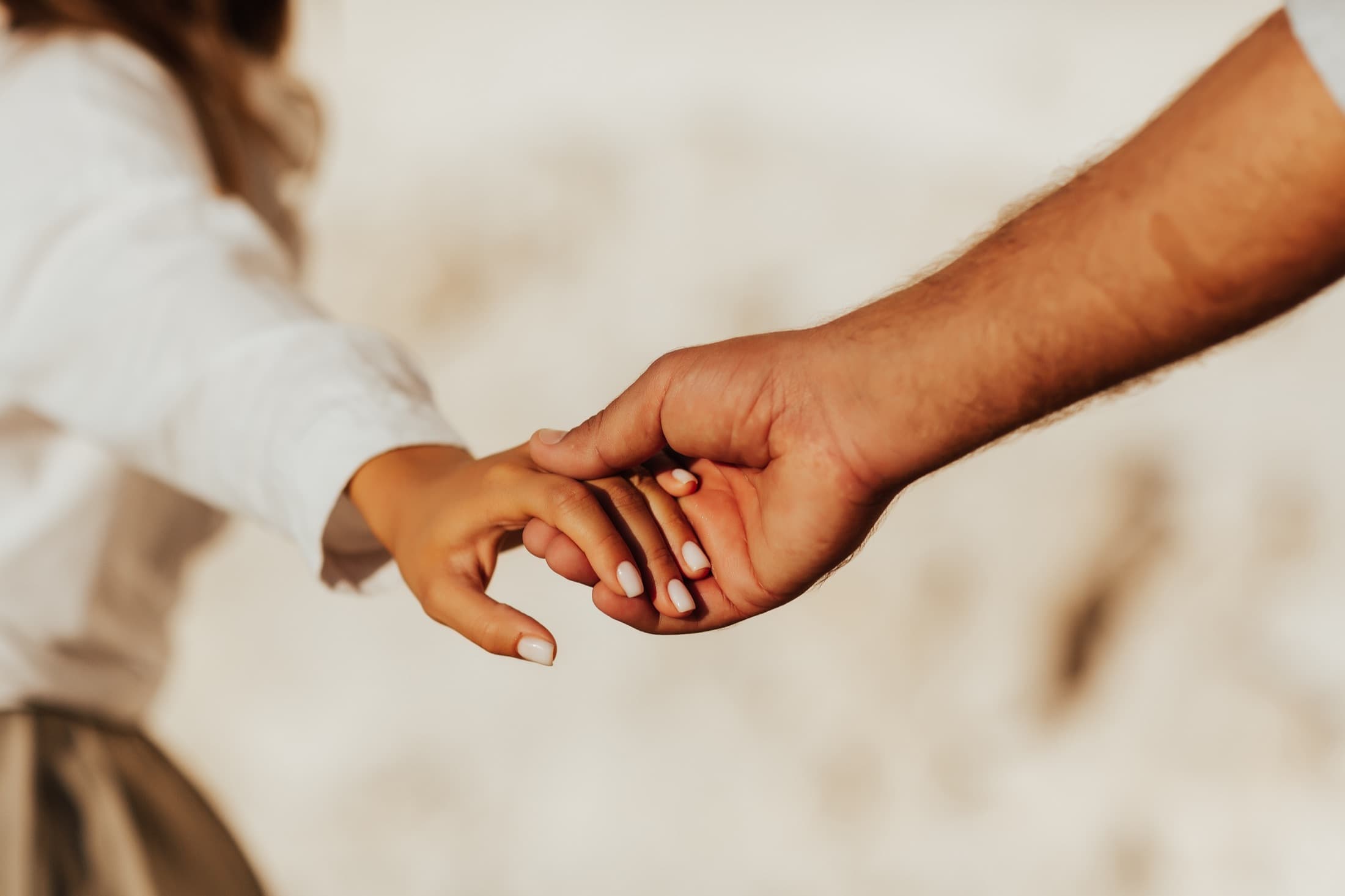 A man and a woman reaching back to hold hands, soft sand behind them